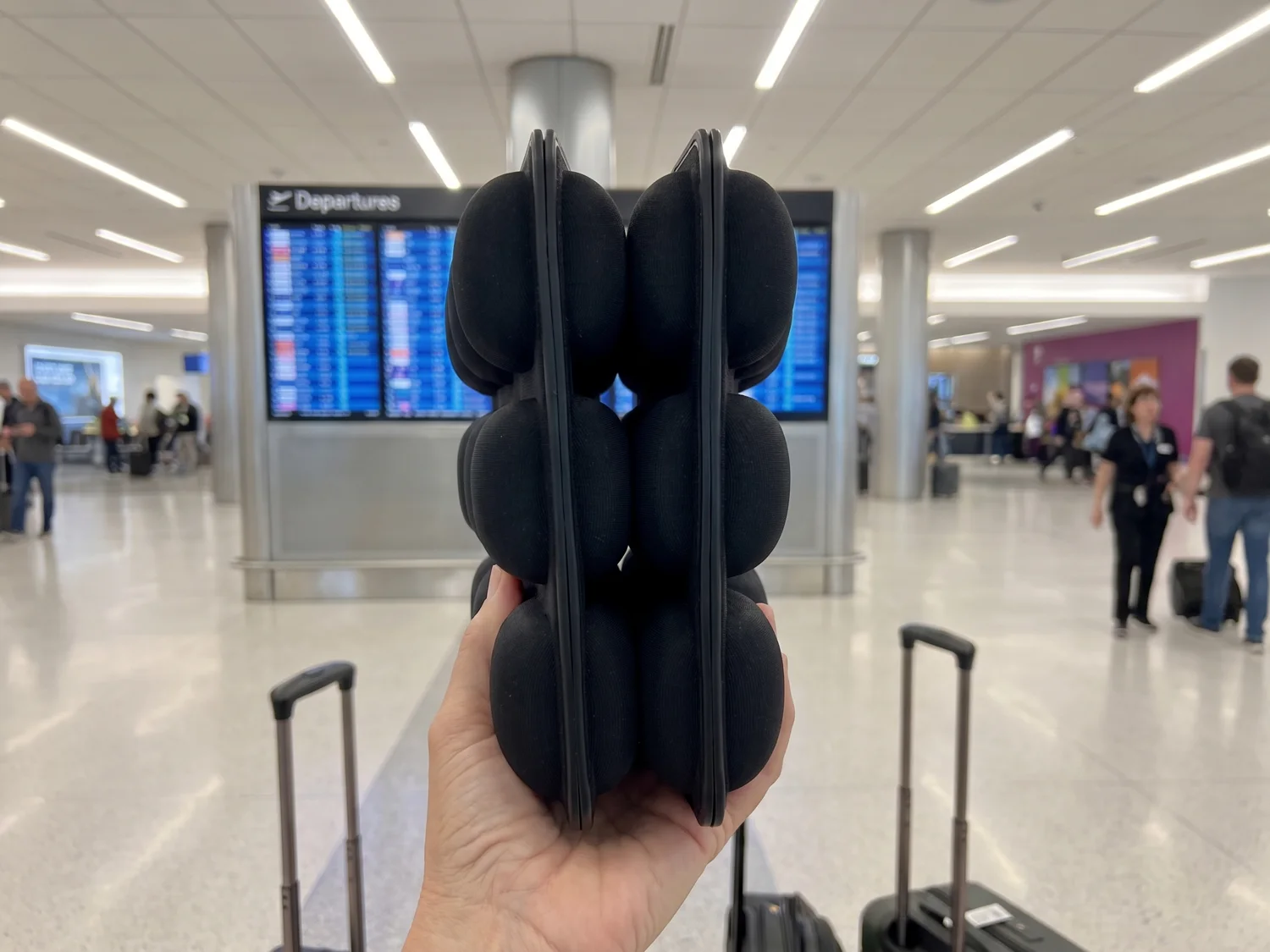 A hand holding the air-cell cushion folded in half, its cells facing outward, ready to clip to a carry-on