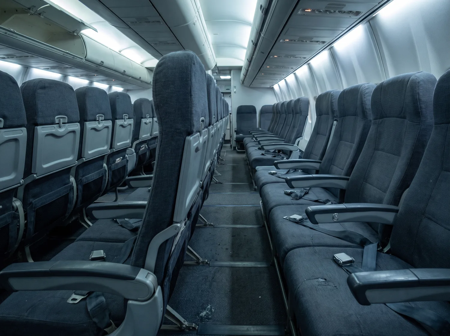An empty economy cabin, rows of thin worn seats with the seatbelts lying across them